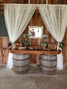 a wooden table topped with two wine barrels under a window covered in white drapes