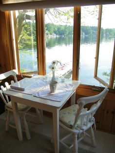 a table and chairs in front of a window overlooking the water with flowers on it