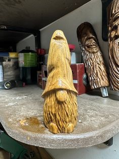 three wooden carved faces on a shelf in a garage, one is wearing a hat and the other has a beard