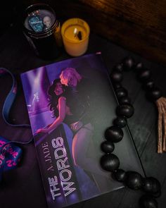 a book on a table next to some beads and candles with a candle in the background