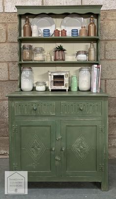 an old green cabinet with many items on it's top and shelves above the hutch