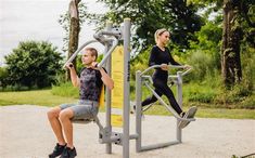 a woman and child doing squats on an exercise equipment in a park setting with trees behind them