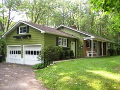 a green house in the woods with two cars parked on the driveway next to it