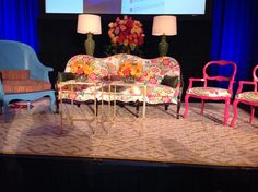 three chairs and two couches on stage with a projector screen in the background