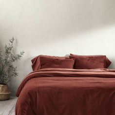 a bed with red sheets and pillows in a room next to a potted plant