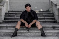 a man sitting on the steps with his legs crossed, wearing black socks and knee high socks