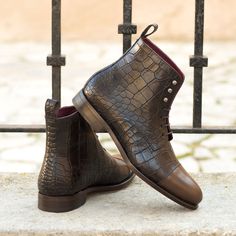 a pair of brown boots sitting on top of a stone slab next to a fence