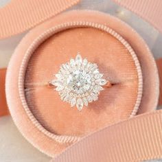 an engagement ring sits on top of a pink velvet box, with ribbon around it