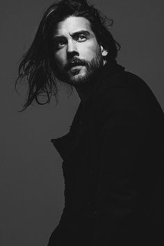 a black and white photo of a man with long hair, wearing a dark coat