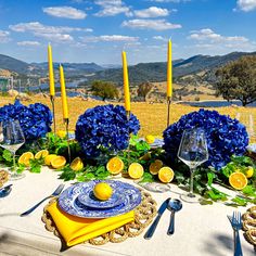 the table is set with blue and yellow flowers, lemons, candles, and plates