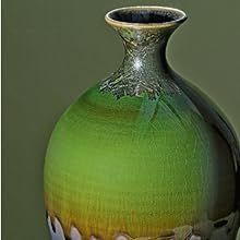 a green vase sitting on top of a table next to a white and black wall