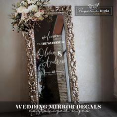 a wedding mirror decorated with flowers and greenery is displayed in front of a wall