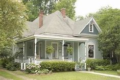 a blue house with white trim and porches in the front yard is surrounded by greenery