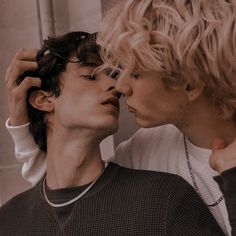 two young men are kissing each other in front of a brick wall and one is wearing a white sweater