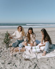 three young women sitting on the beach with presents in their hands and one holding a christmas tree