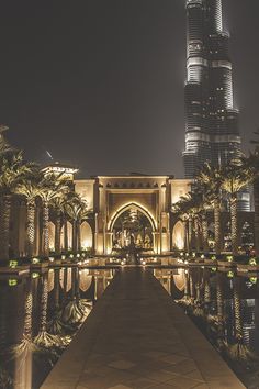 the burj building is lit up at night with its reflection in the water