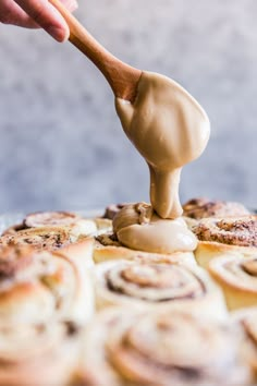 someone is dipping icing onto some cinnamon rolls