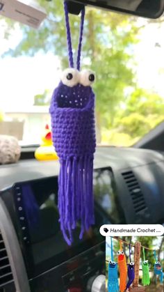 a purple crocheted cell phone holder hanging from the dashboard of a car with eyes on it