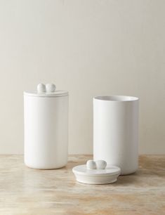 two white ceramic containers sitting on top of a table next to each other with lids