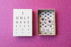 an open box with eyeballs inside on a pink surface next to a card that says i only have eyes for you