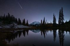 the night sky is reflected in a still lake with trees and mountains in the background