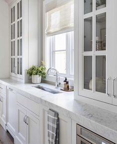 a kitchen with white cabinets and marble counter tops