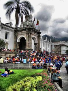 many people are sitting on the grass in front of an old building with palm trees