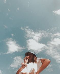 a woman in a hat talking on her cell phone under a blue sky with white clouds