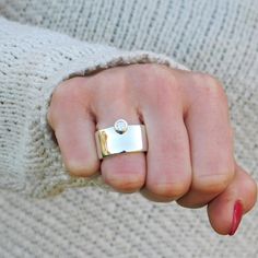 a woman's hand wearing a gold and silver ring with a diamond on it