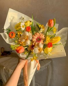 a bouquet of flowers is being held up by someone's hand in front of a wall