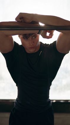 a young man is holding his hands behind his head and looking at the camera while standing in front of a window