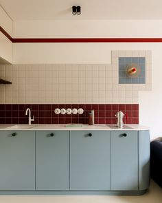 a kitchen with blue cabinets and red tiles on the wall, along with white flooring