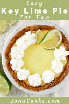 a pie with limes and whipped cream on top sits next to a fork, knife and two slices of lime