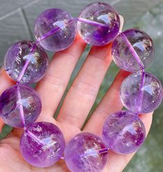 a hand holding five purple glass beads in it's palm, with one being held up to the camera