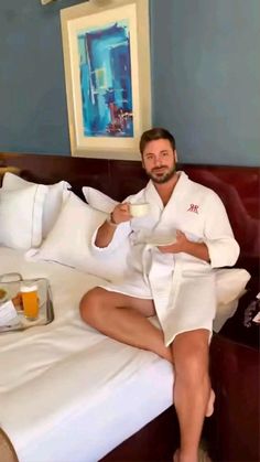 a man sitting on top of a bed holding a cup