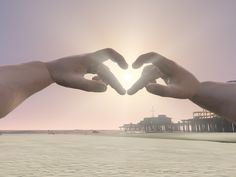 two hands making a heart shape on the beach