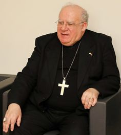 an older man sitting in a chair with a cross on the back of his jacket