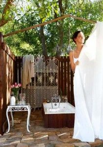 a woman standing in front of a bath tub next to a wooden fence and table