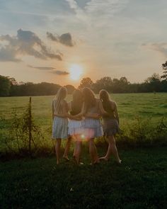 three girls standing in the grass with their arms around each other as the sun sets