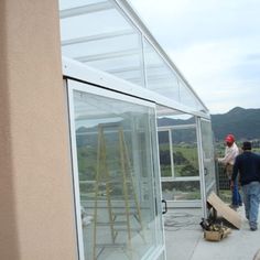 two men working on the side of a building with glass walls and doors that are open