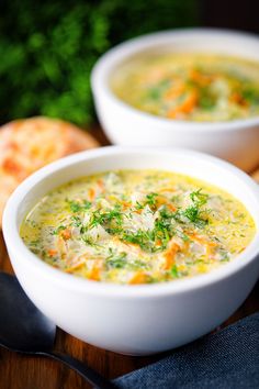 two white bowls filled with soup sitting on top of a wooden table next to bread