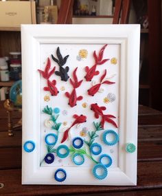 a white frame with red, blue and green fish in it on top of a wooden table