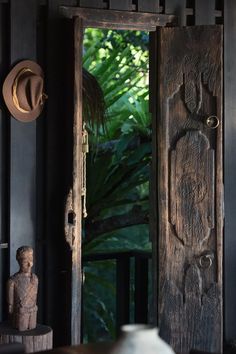 an open wooden door leading to a lush green jungle area with a statue in the foreground