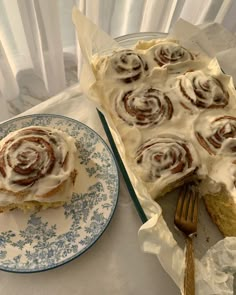 a plate with some food on it next to a pan filled with cinnamon rolls and a fork