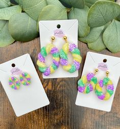 three pairs of colorful earrings sitting on top of a wooden table next to green leaves