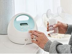 a woman is holding a baby bottle in front of an automatic breast pump that's on top of a table