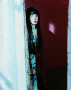 a woman with long black hair standing in front of a red and white wall wearing a colorful dress