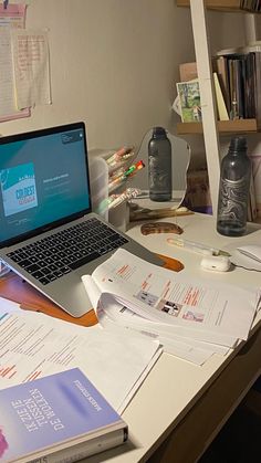 an open laptop computer sitting on top of a wooden desk next to books and papers