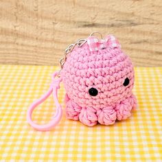 a pink crocheted keychain sitting on top of a yellow and white checkered table cloth