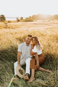 a man and woman sitting on the ground in tall grass with their arms around each other